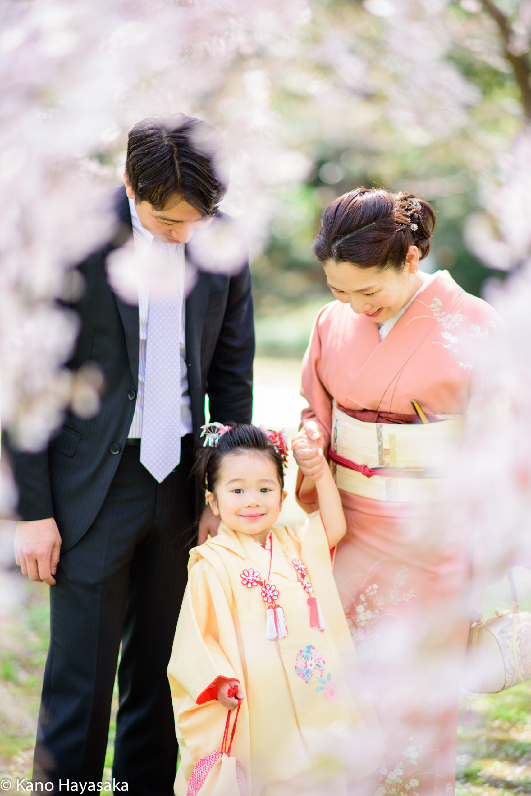 桜の下で七五三のお参りをする家族三人