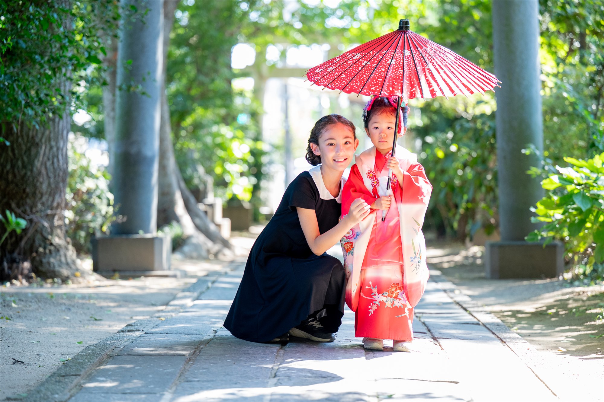 鳥居の参道で和傘をさす七五三の姉妹