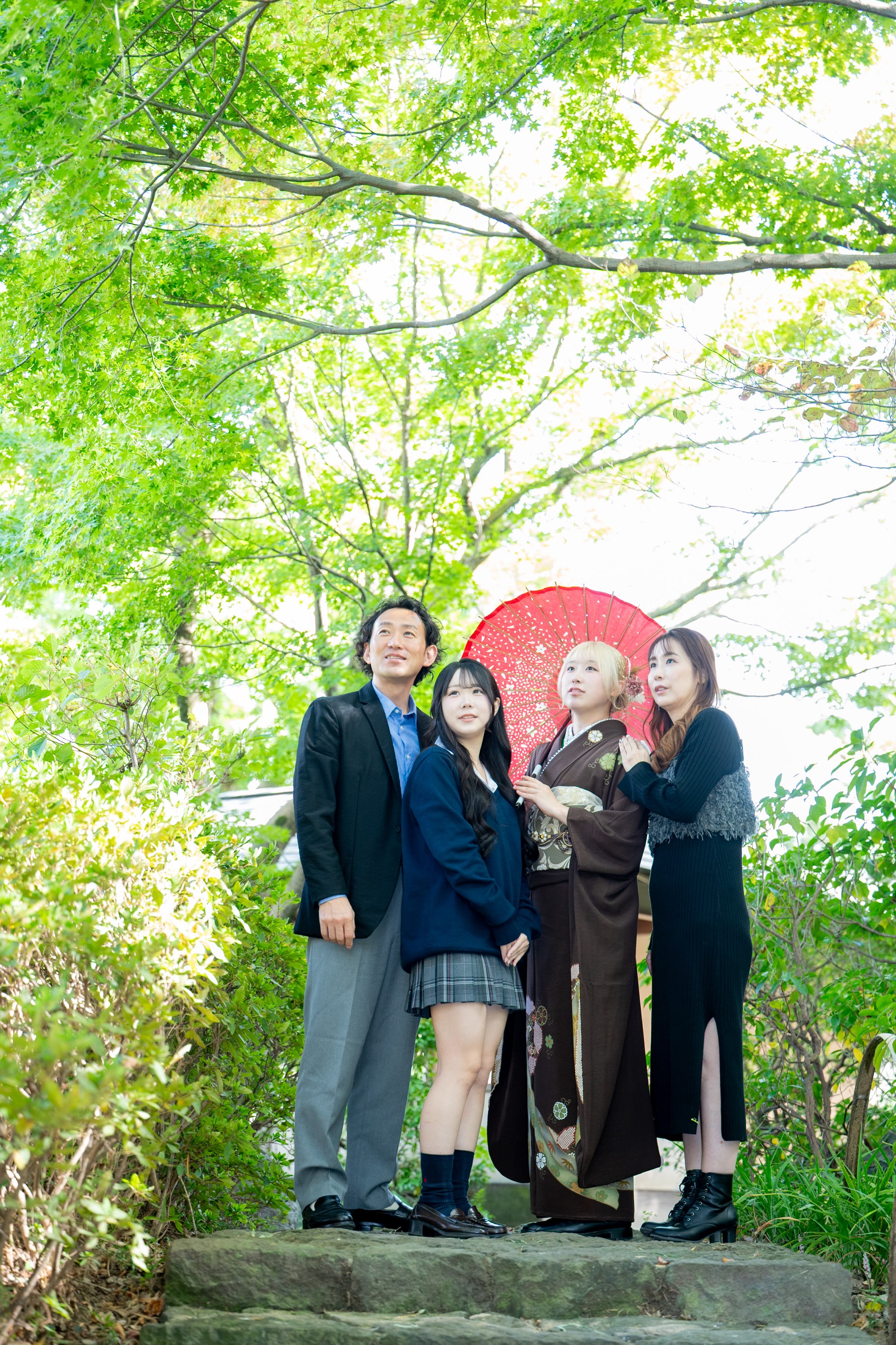 花田苑の新緑の下で、成人式の振袖姿の娘さんとご家族が空を見上げる家族写真