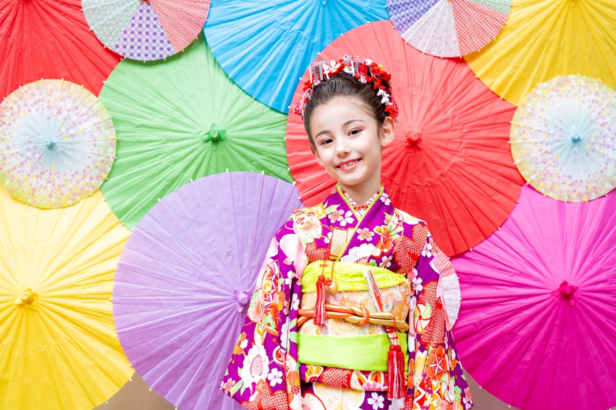 カラフルな和傘を背景に笑う7歳の七五三の女の子