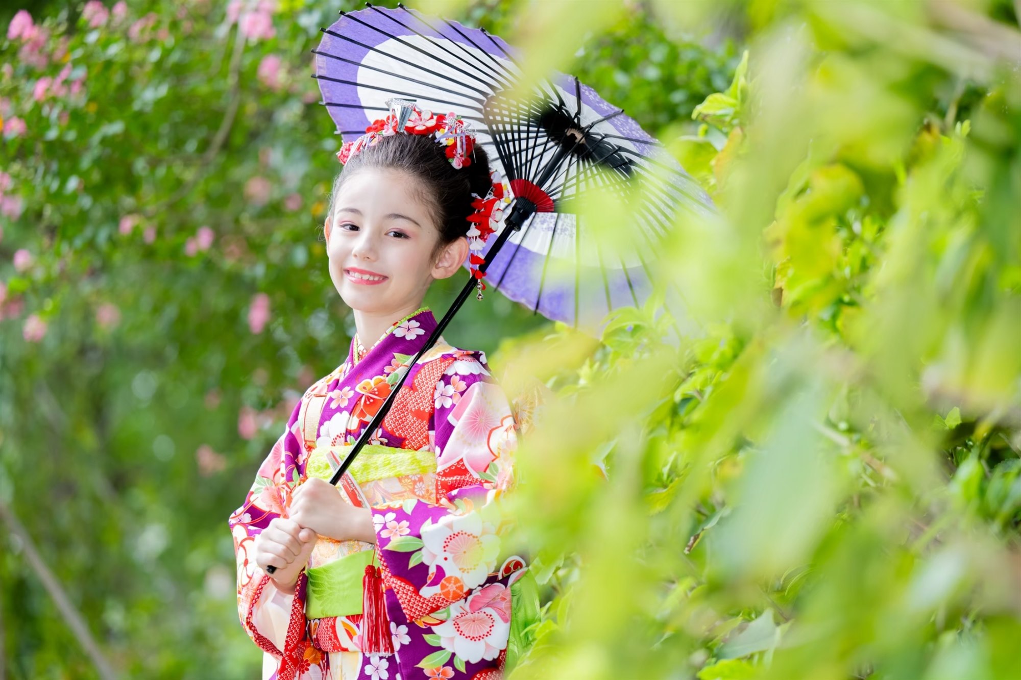 緑のなかで和傘をさして笑う7歳の七五三の女の子